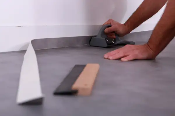 Pose lino : un artisan utilise un outil pour bien aplatir le revêtement de sol gris près du mur.