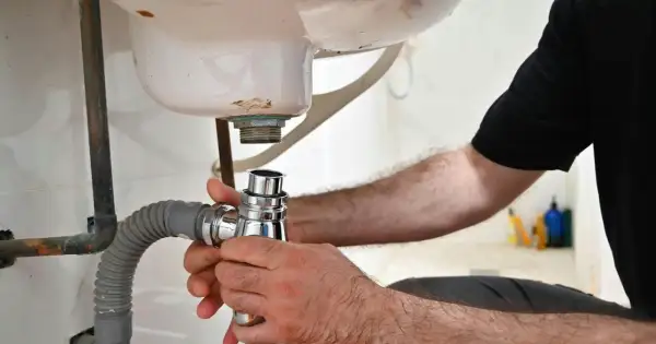 Main tenant en main le siphon, il procède au démontage du siphon de la baignoire pour une réparation.
