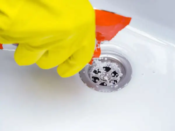 Gant jaune versant des granulés dans un siphon de douche pour déboucher la douche.